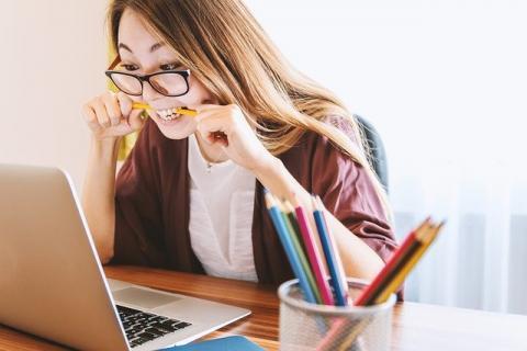 studentka w okularach siedzi przed komputerem i przygryza nerwowo ołówek